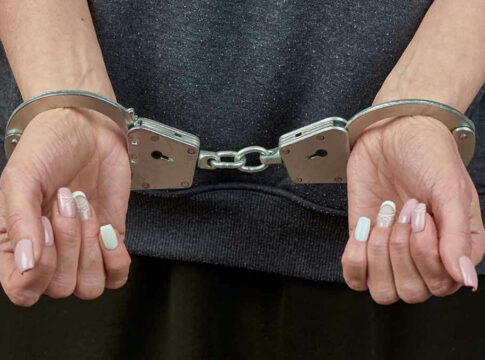 Handcuffed person with painted nails in dark clothing.