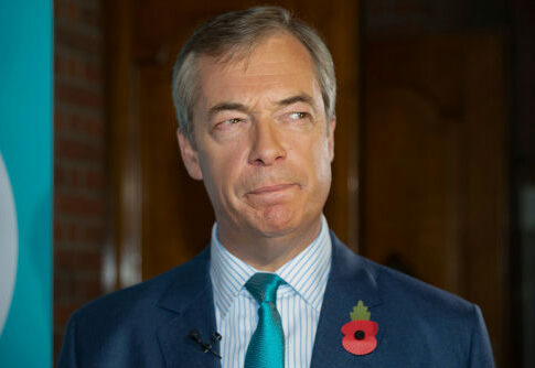 man in suit with teal tie and red poppy pin looking to the side