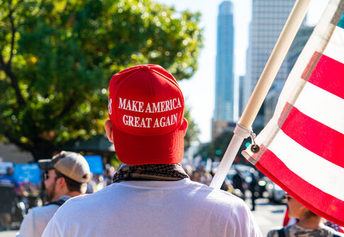 Person wearing a red Make America Great Again hat holding an American flag at a rally