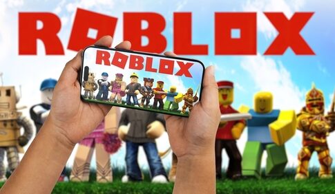Hands holding a smartphone displaying the Roblox game with characters in the background