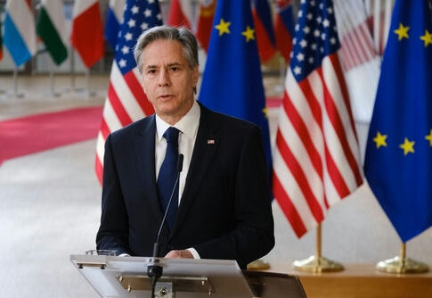 Man in suit speaking at podium with international flags behind