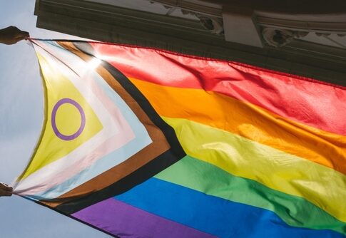 Hands holding a colorful pride flag against a bright sky