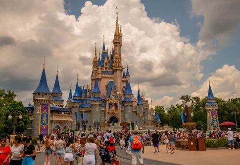 Crowd of visitors in front of a large Disney castle under a cloudy sky