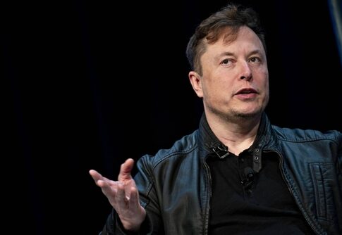 A man in a black leather jacket speaking at a conference