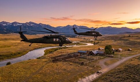 Two military helicopters flying over a rural landscape at sunset