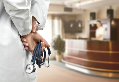 A doctor holding a stethoscope behind their back in a hospital reception area