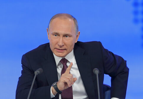 A political leader speaking at a press conference with a serious expression