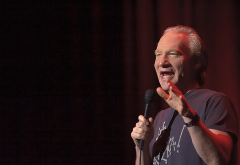 A comedian performing on stage with a microphone in hand